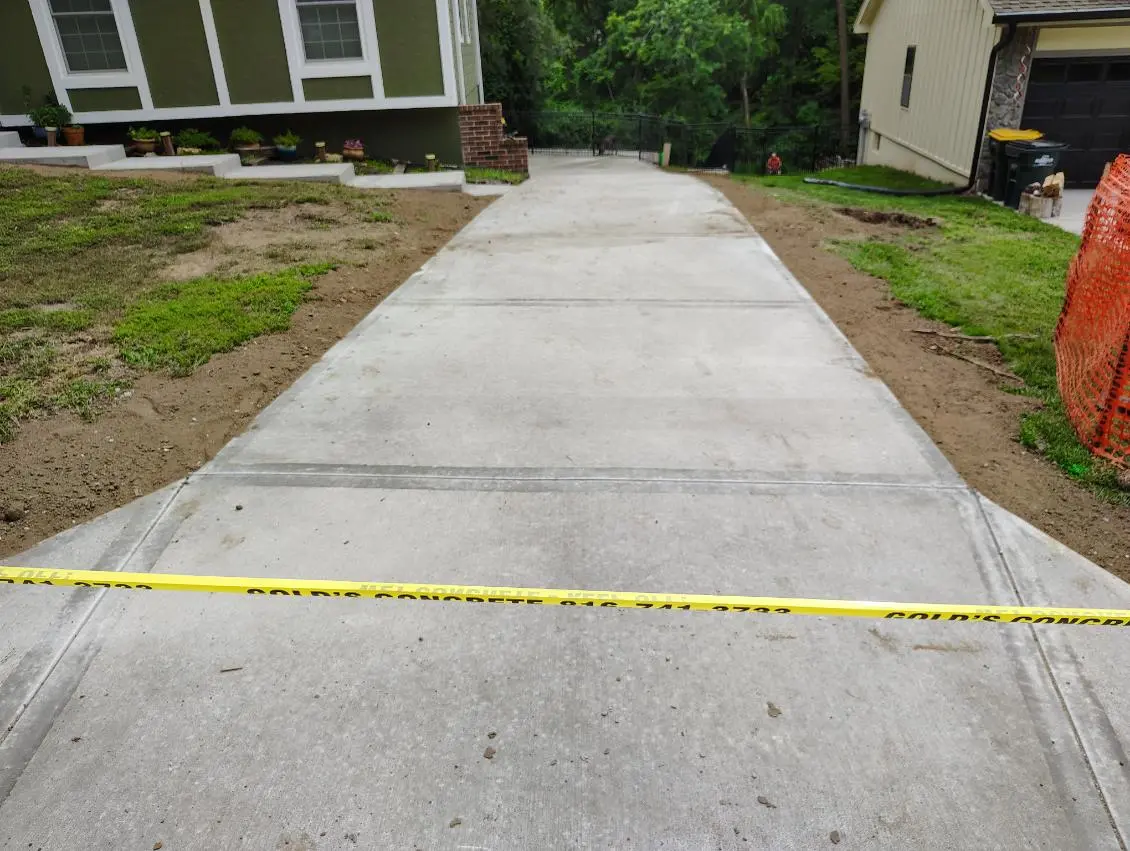 freshly finished concrete driveway bordered by grass and caution tape at a residential property