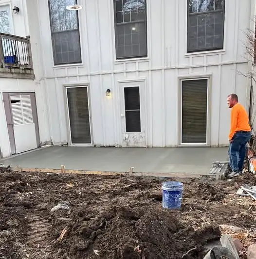 worker finishing freshly poured concrete patio behind a residential house
