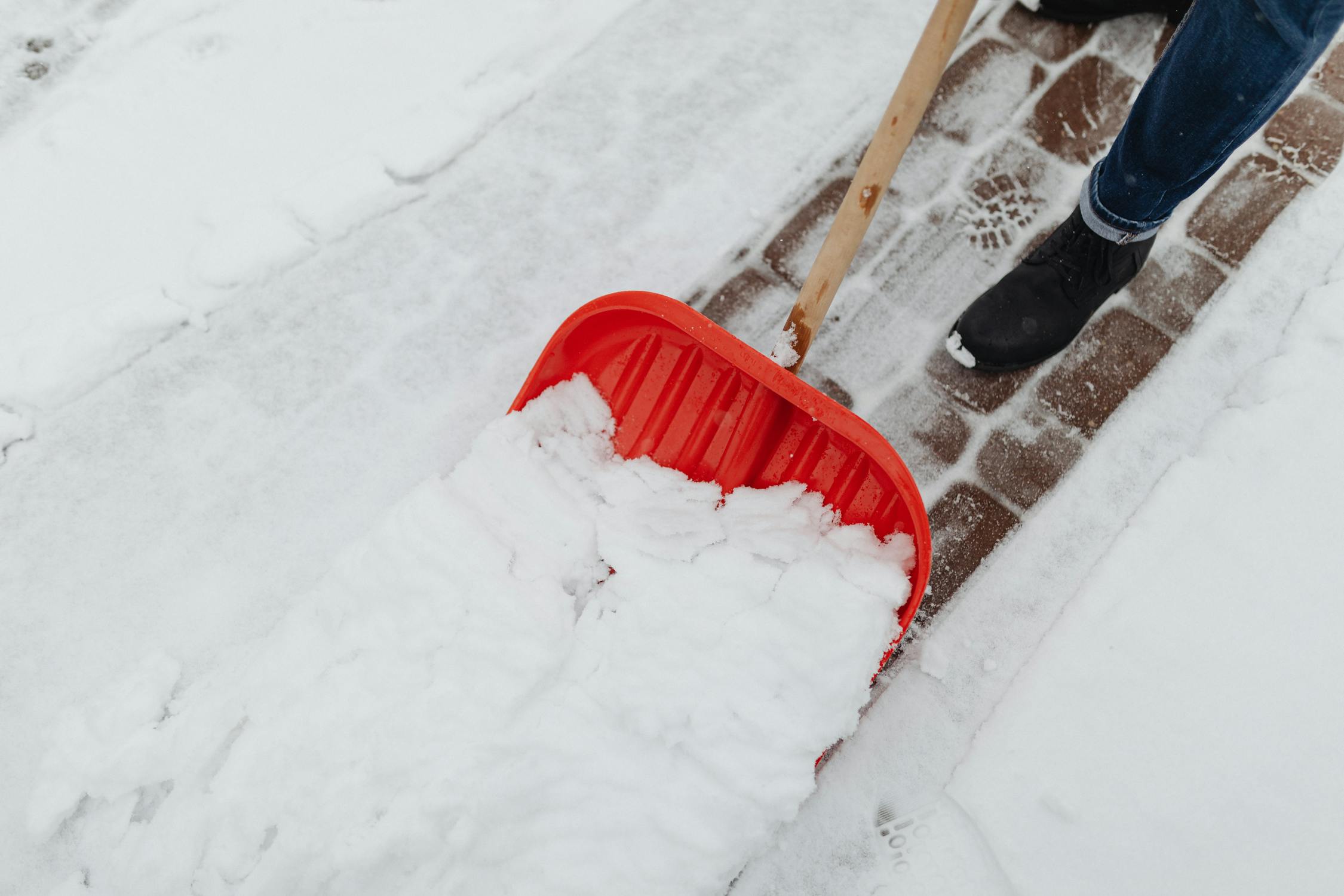 Homeowner shoveling snow from a concrete driveway with a plastic shovel during Kansas City winter